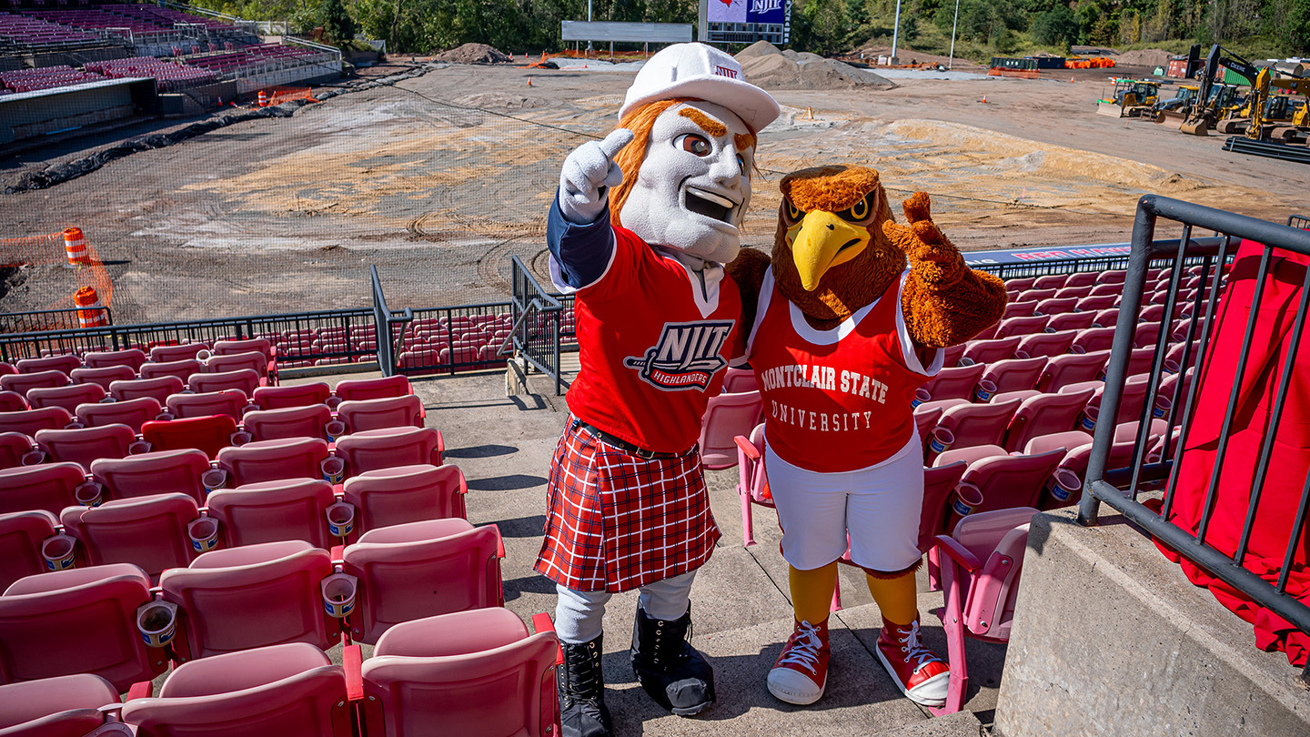 Rocky the Red Hawk and the NJIT Highlander pose among stadium seats.