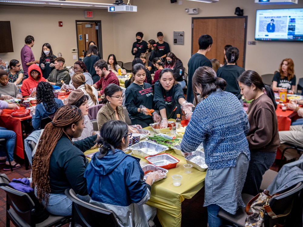 Students seated at tables women unwrap ingredients to prepare to make kimchi.