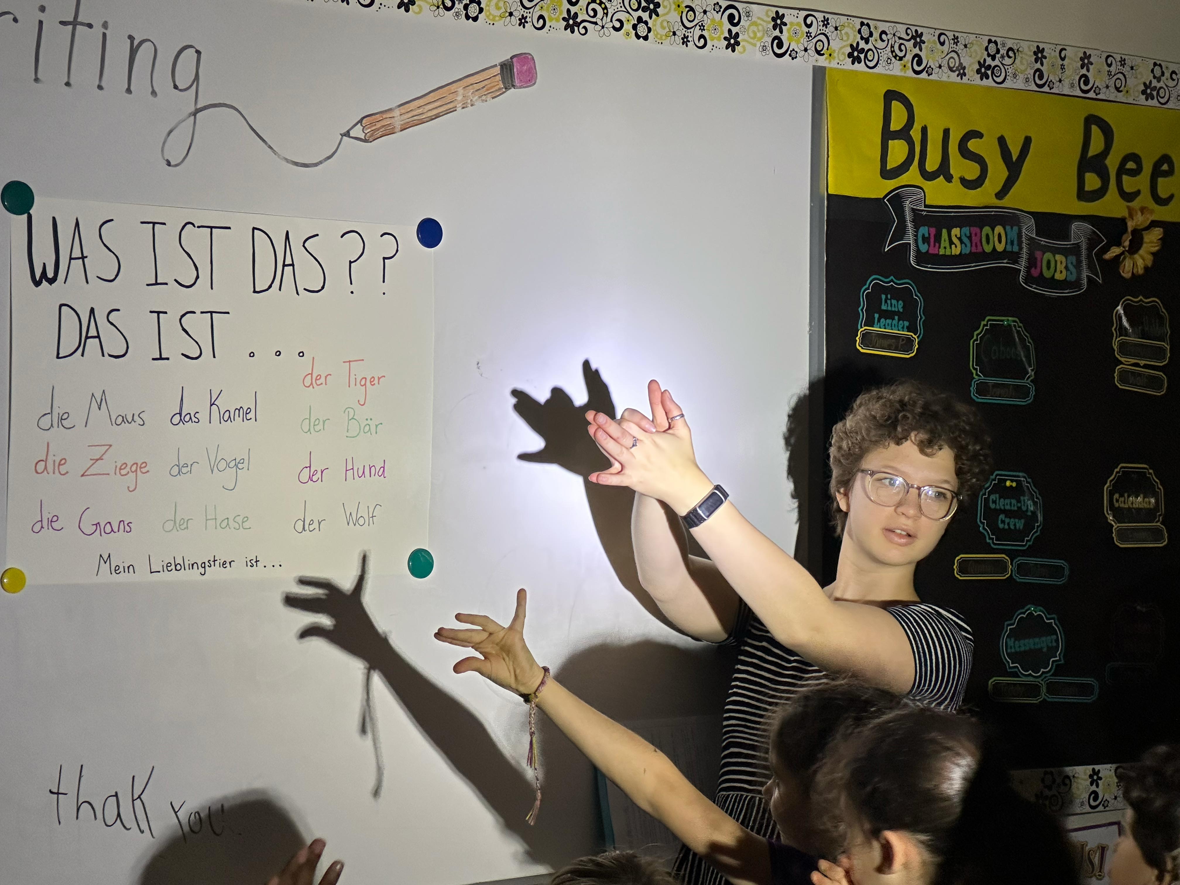 student in classroom standing in front of whiteboard making shadow puppets