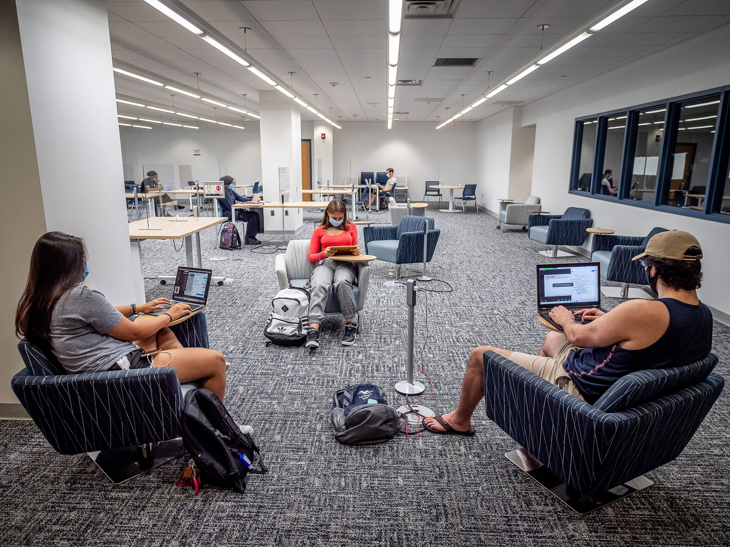 Students sit at distanced chairs in lounge using laptops