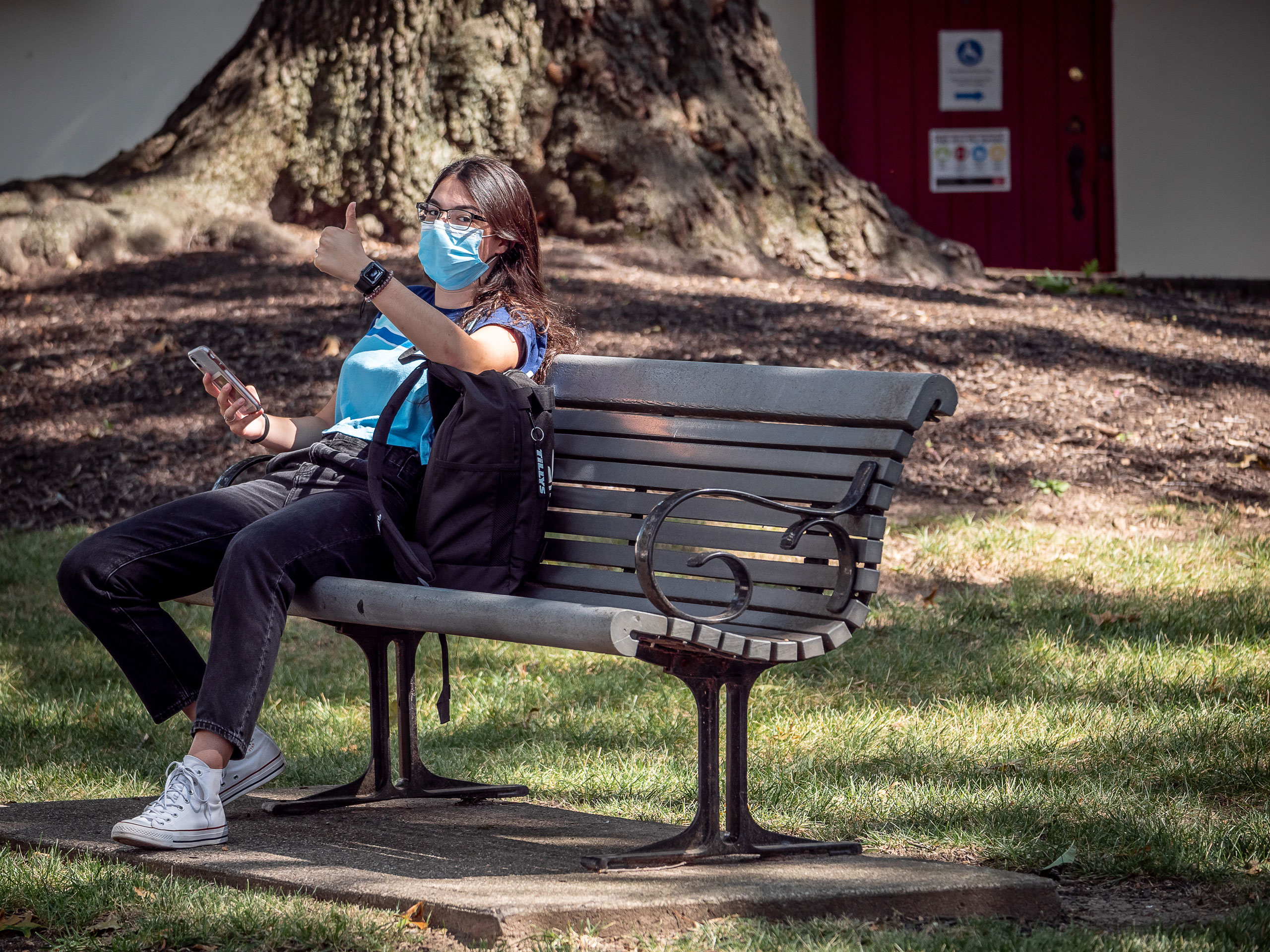 Student on bench spots our photographer and gives him a thumbs-up