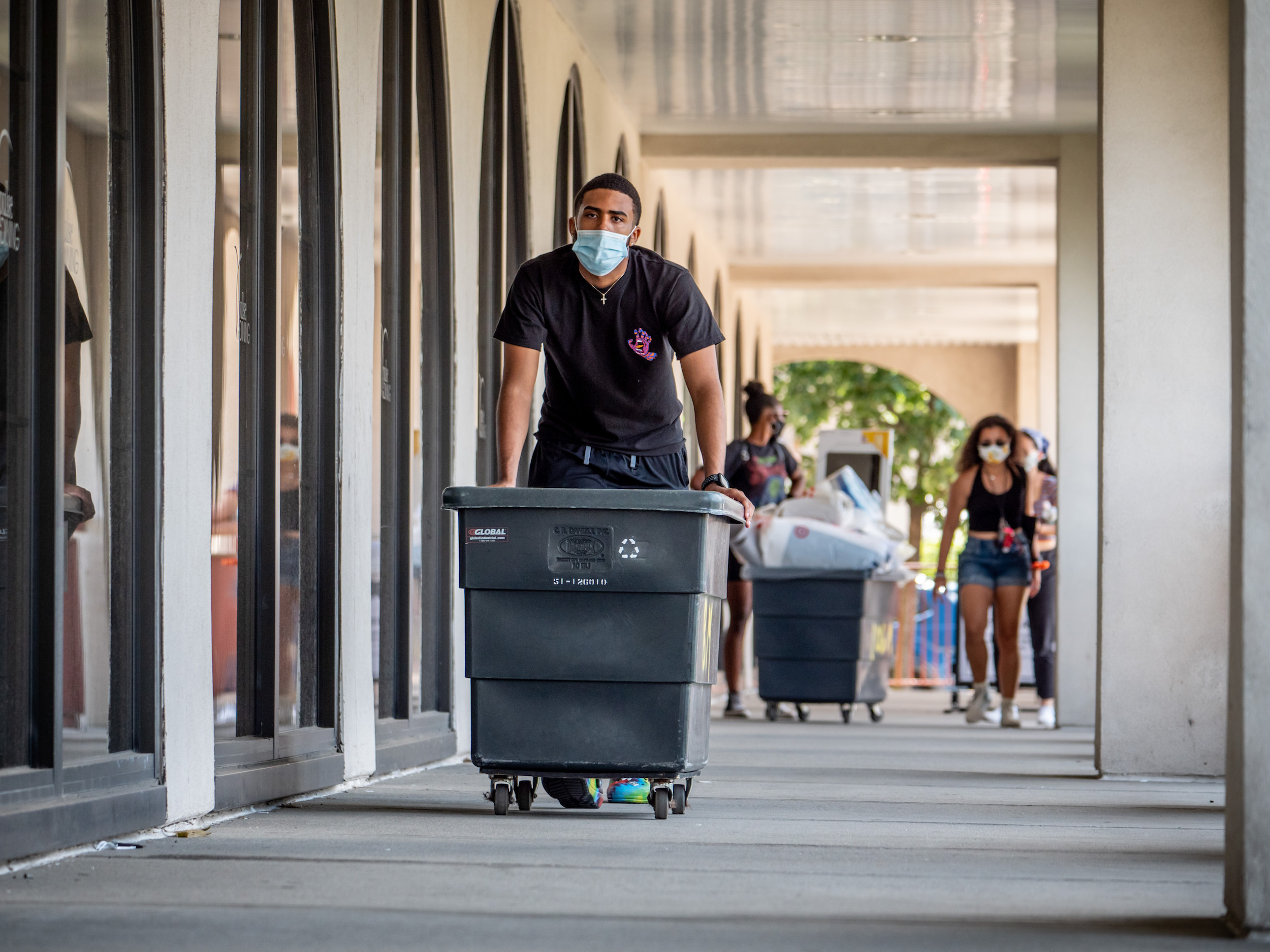 Students pushing wheeled carts into a building while moving into campus