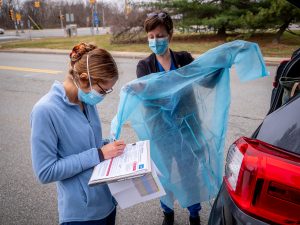 nurses unpacking PPE from the trunk of a car and putting on paper gowns