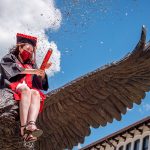 graduate on top of hawk statue setting off confetti
