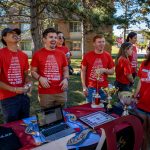 Four students at table on quad wearing red shirts