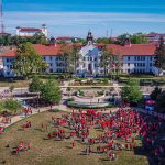Aerial view of red-shirted students on the historic quad with Cole Hall behind them