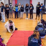 Students cut fabric on the floor as others gather around.