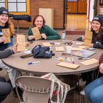 People sit around a table holding decorated paper bags.
