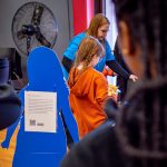 Young girl looking at information on table with two college students in the foreground