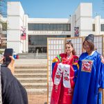 Two students try on traditional Korean garments and pose for a photo in front of the Student Center