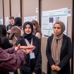 A man talks to two students in hijab about their research poster about annotating the genomes of sea phages.