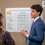  A student in a suit and tie points to his research poster about misinformation and the First Amendment.