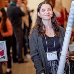  A student smiles as she carries her rolled up research paper at the end of the symposium.