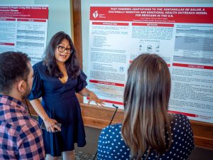 A student gestures as she speaks to two onlookers in front of a poster.