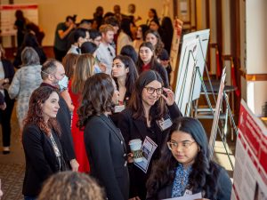 Many students stand in front of posters in a large conference room.