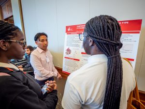 A student stands in front of a poster as two people look on.