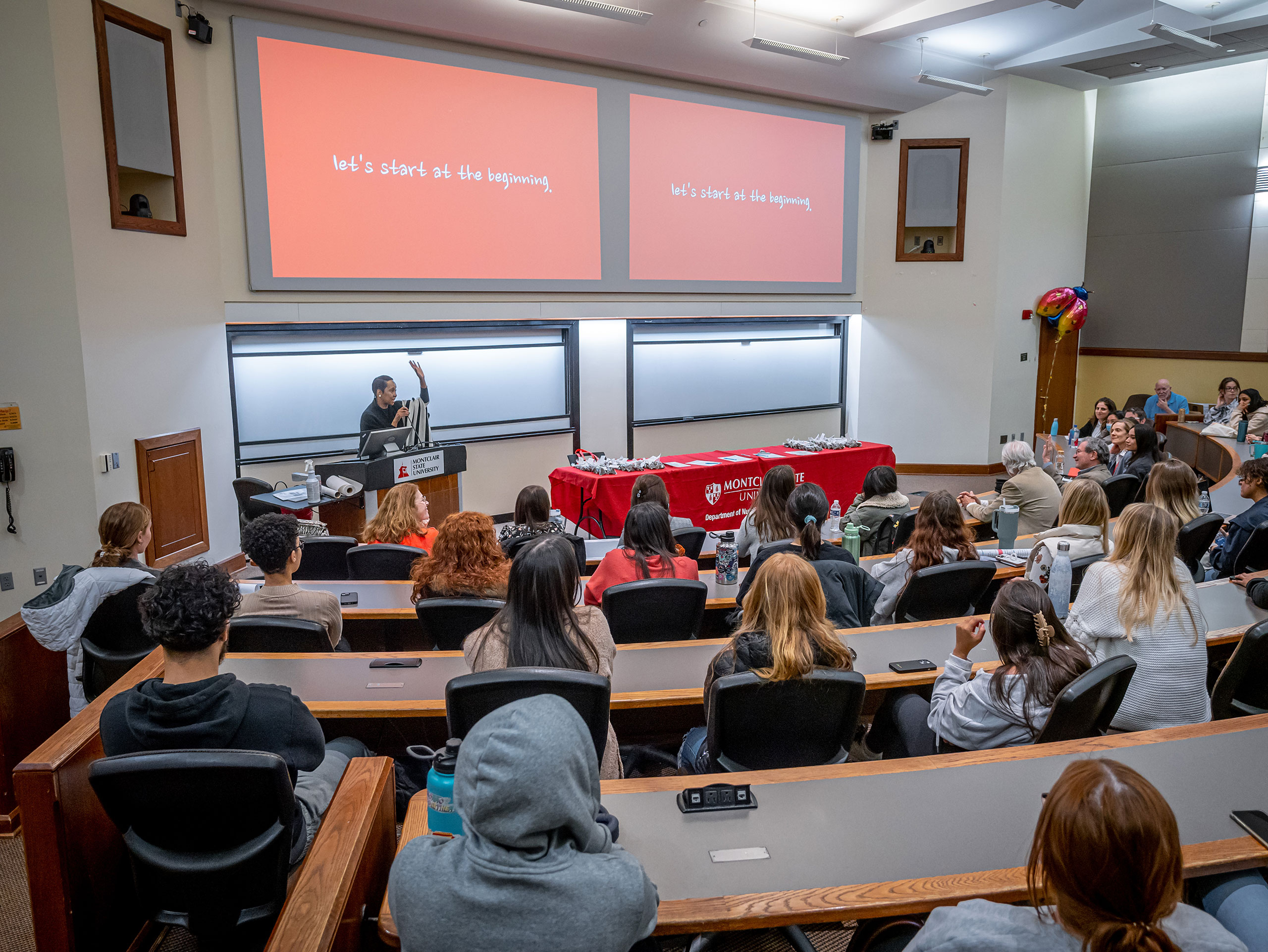 A woman speaks in front of a classroom full of students.