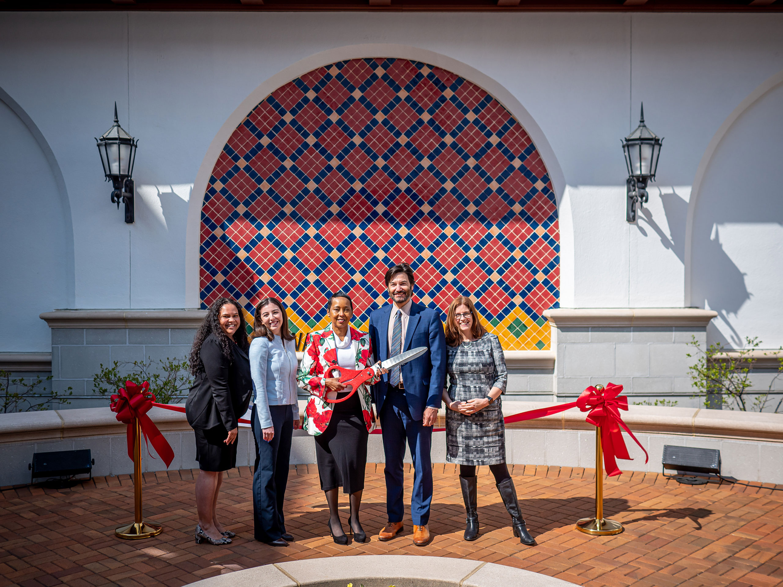 A woman holding a pair of oversized scissors is flanked by three women and a man.