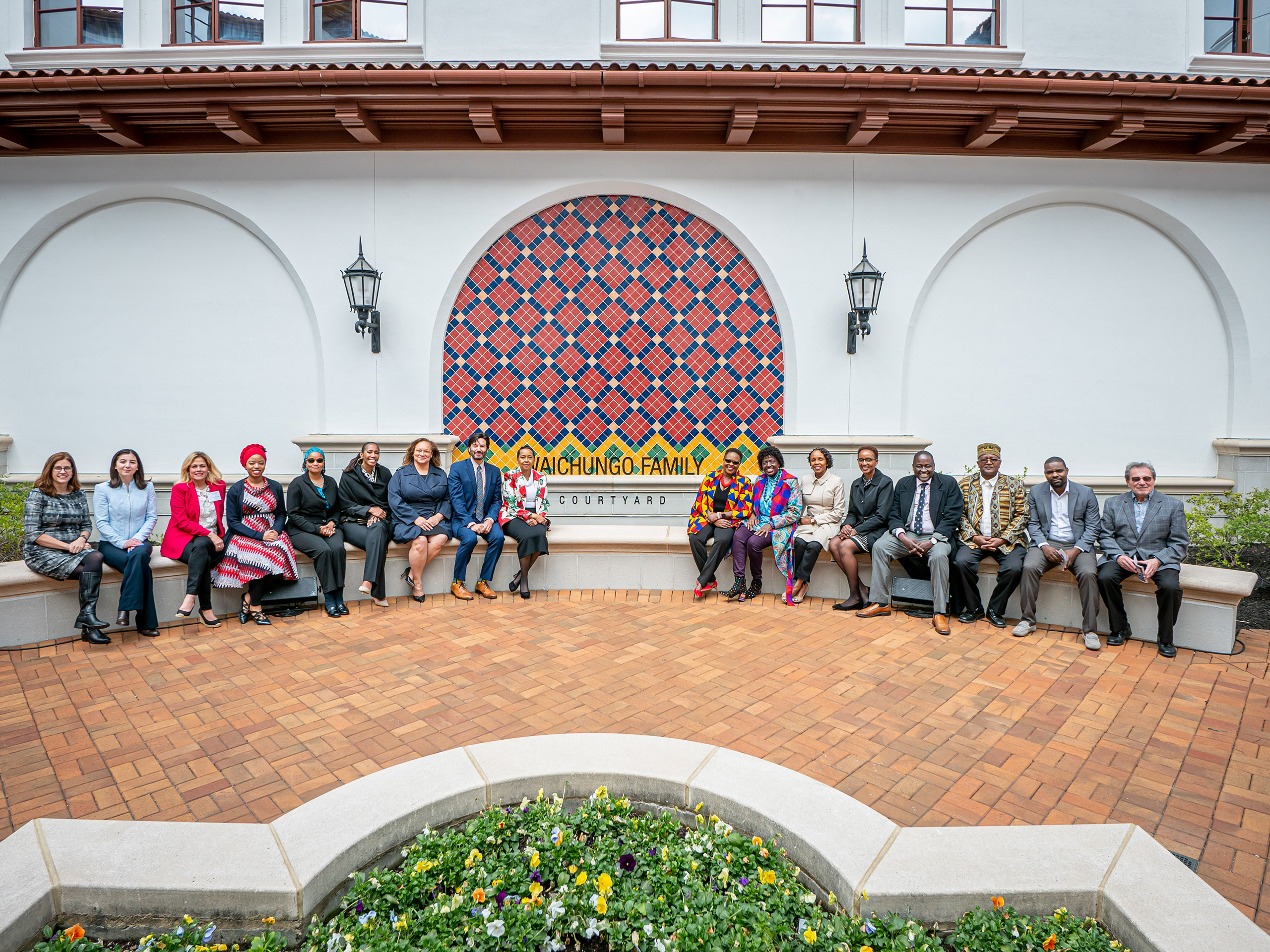 17 people pose in front of the Waichungo Family Courtyard mosaic sign.