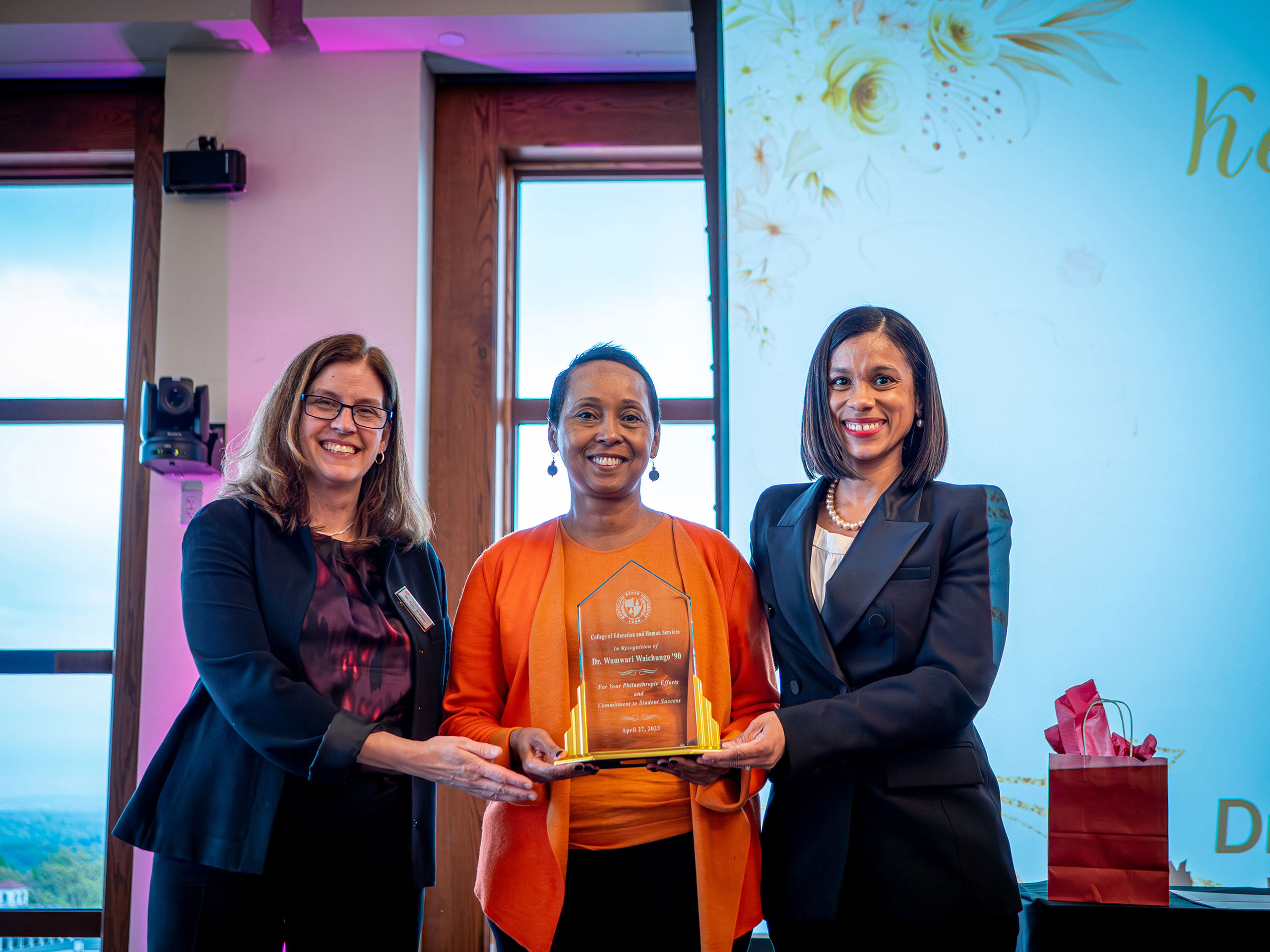 Three women smile as they hold an award.