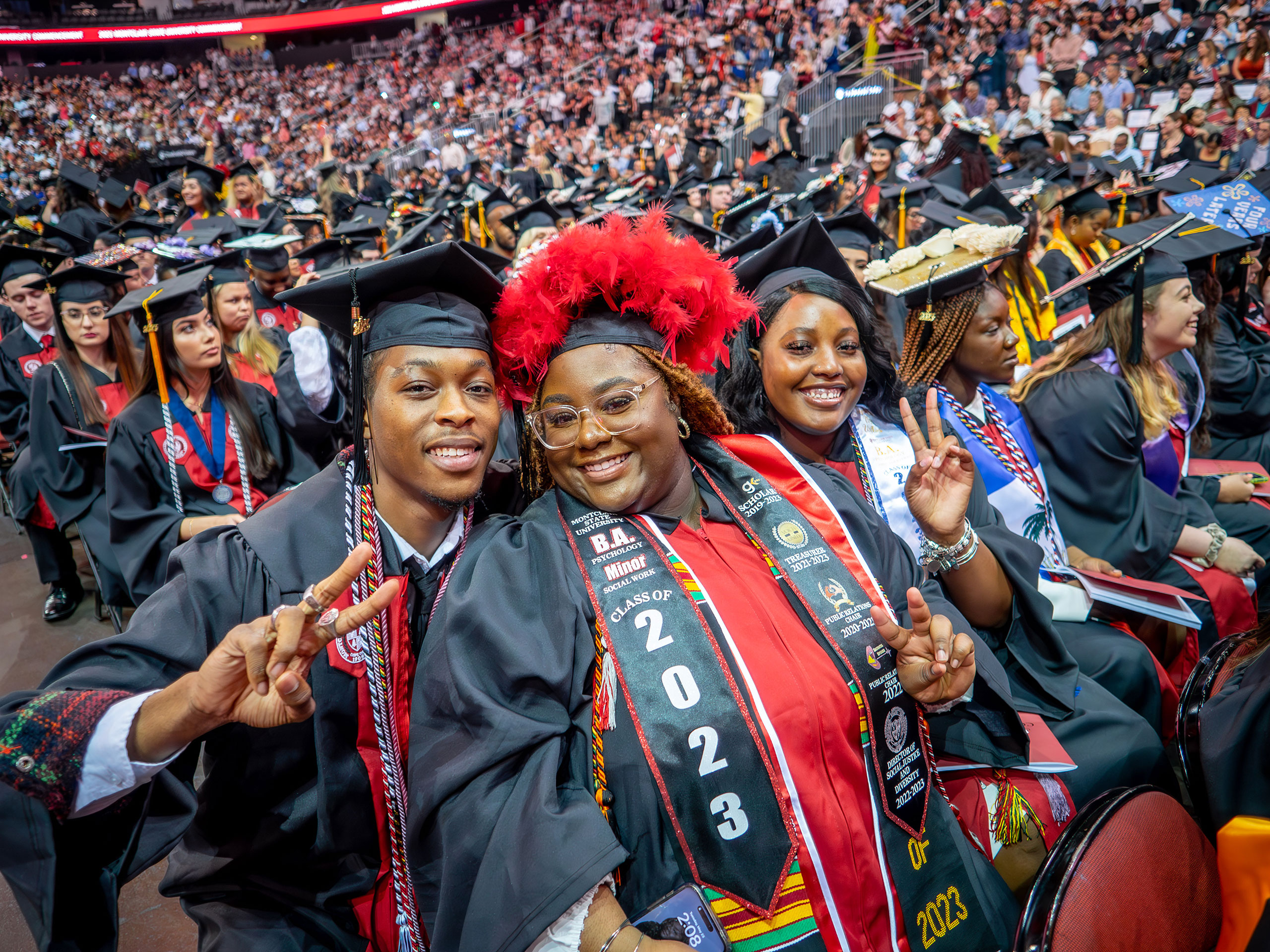 three graduates smile and hold up peace gestures at the camera