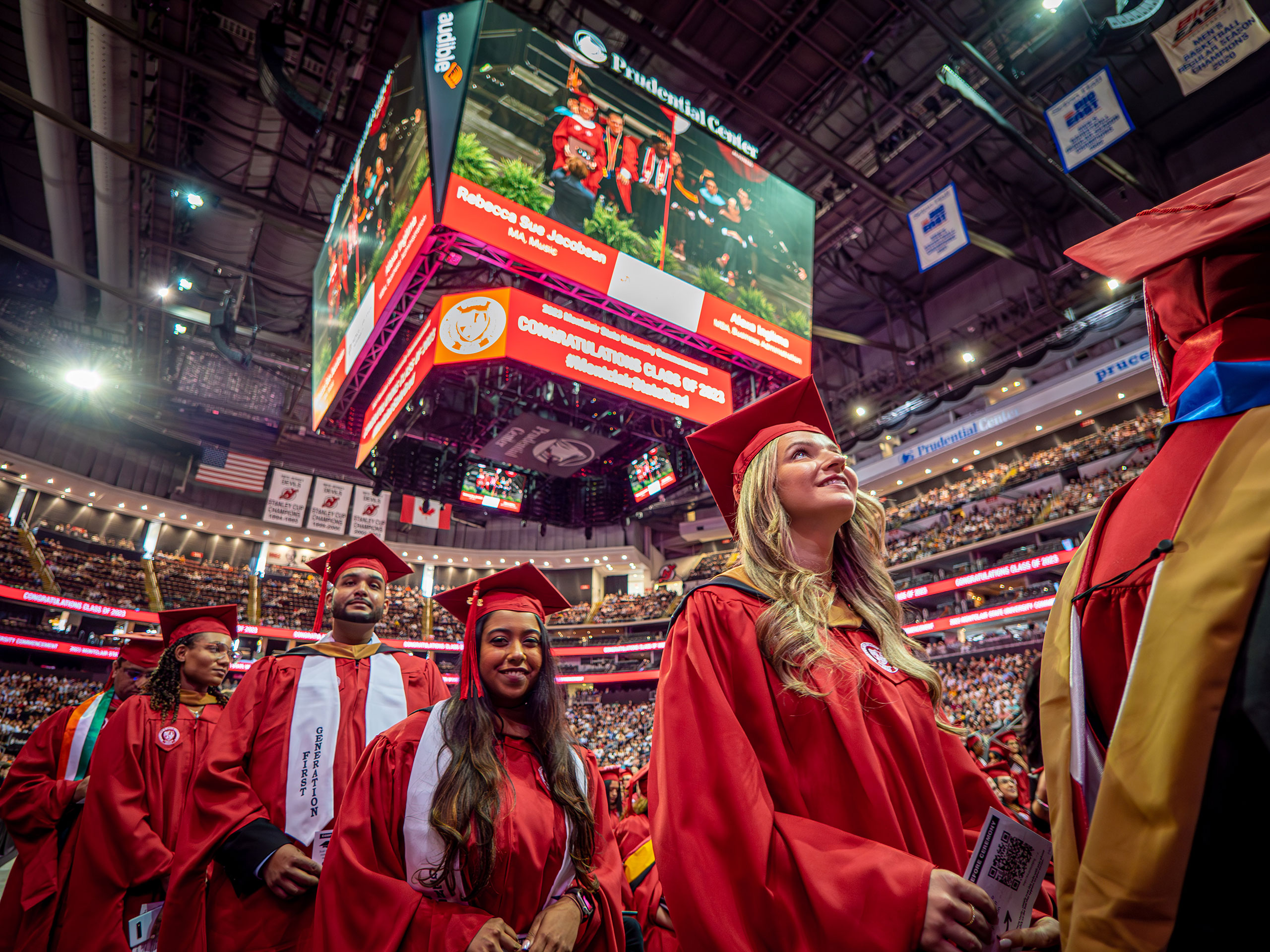 graduates in red caps and gowns line up as they walk toward a stage