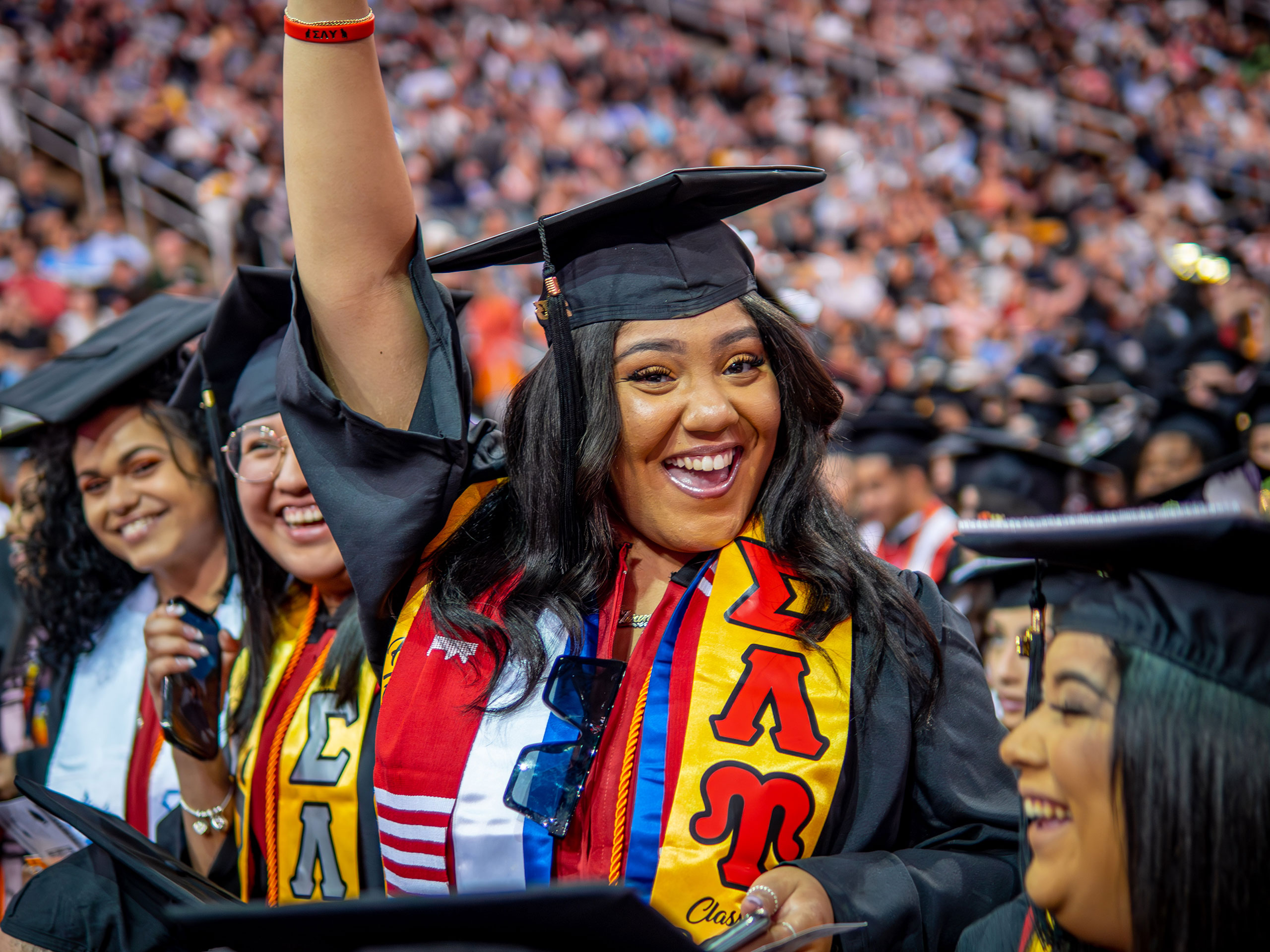 a graduate smiles, wearing a stole with the Greek letters Sigma Lambda Upsilon