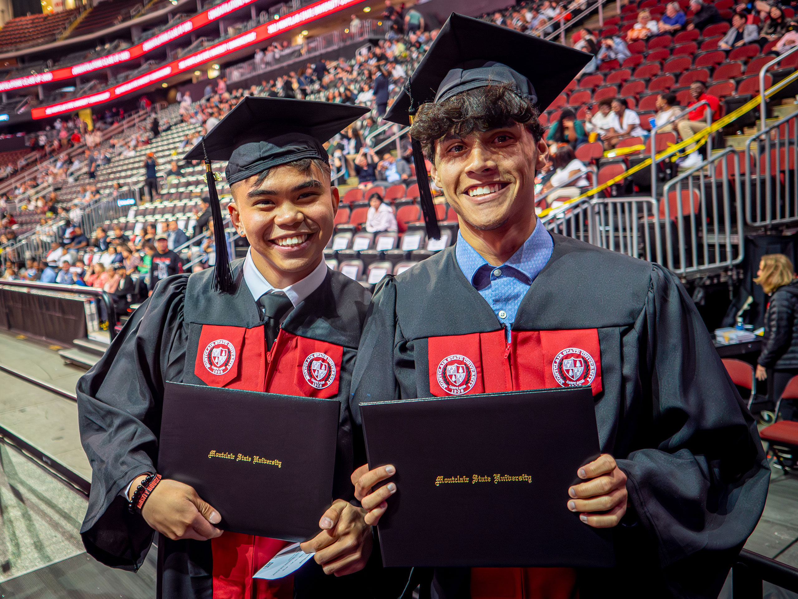 Two graduate smile and hold diploma covers