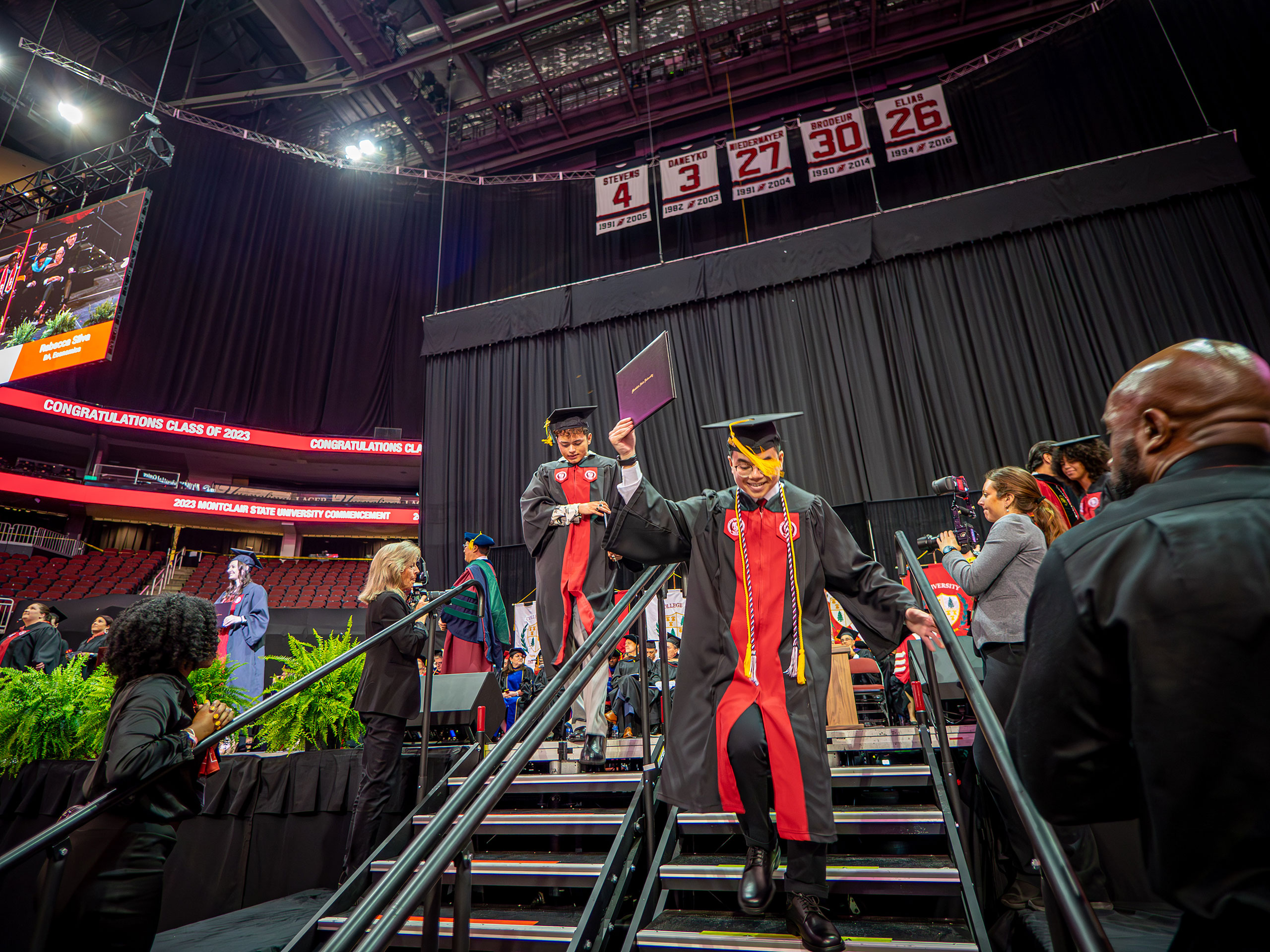 graduate walking down stairs from stage, holding diploma up