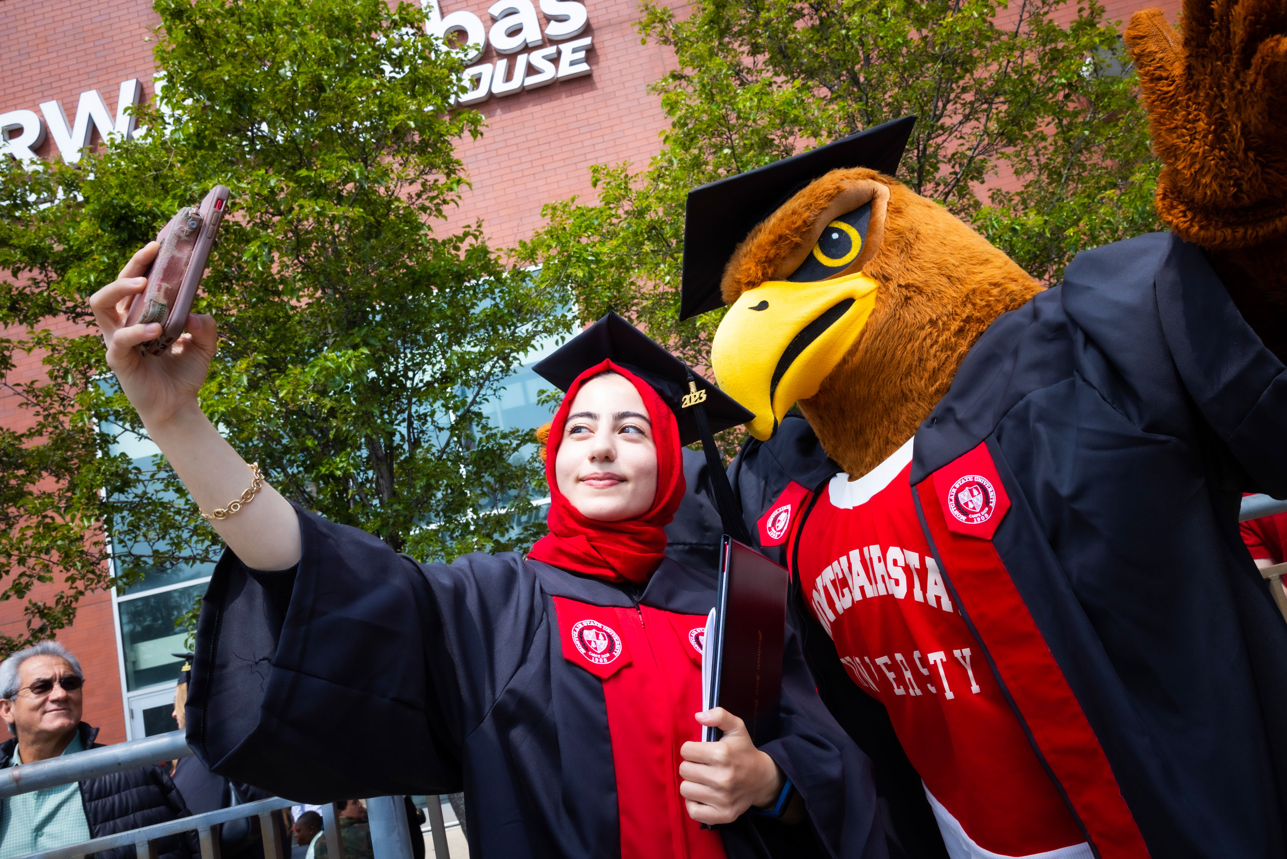 graduate posing with university mascot in cap and gown