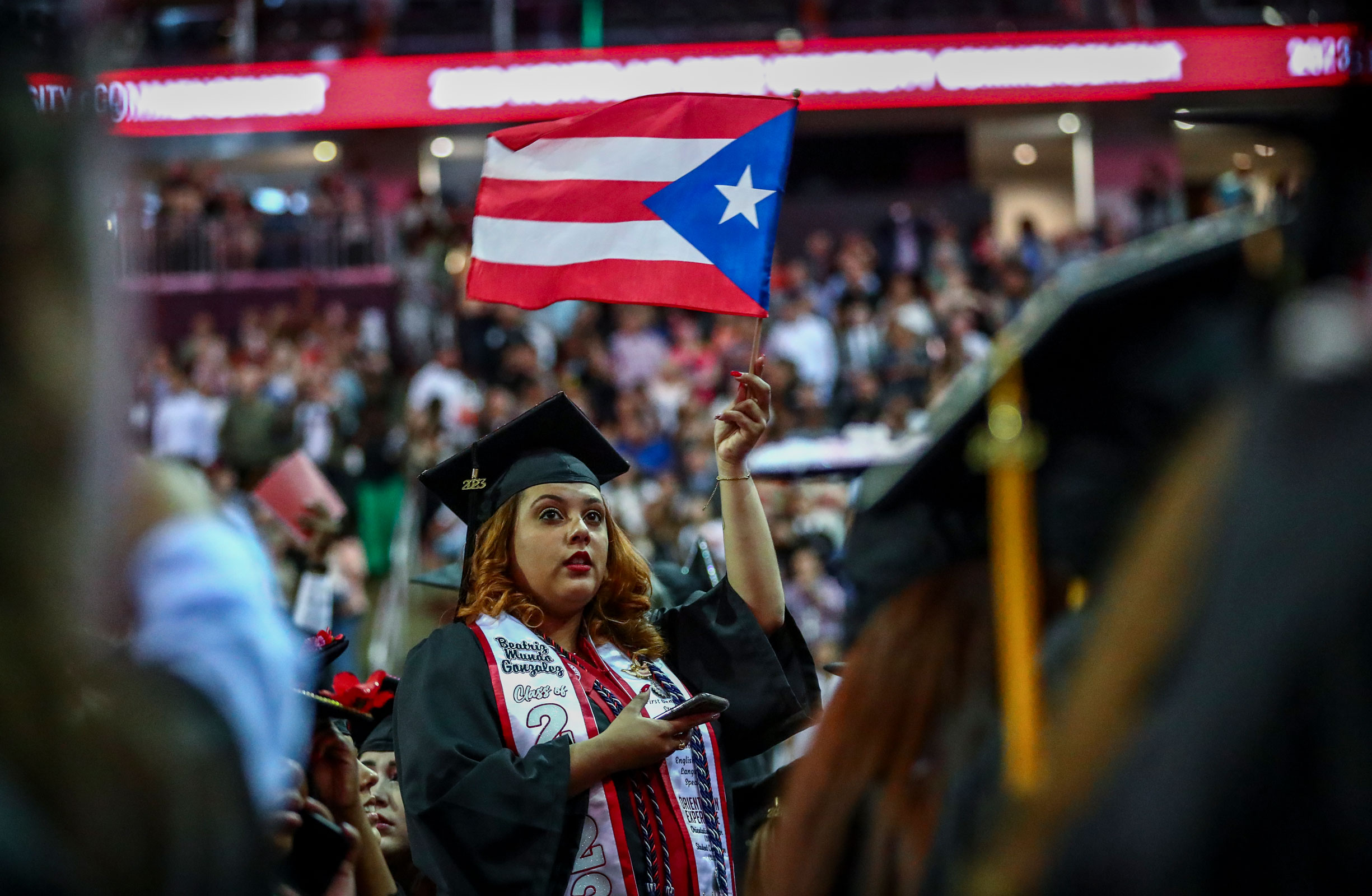 graduate in cap and gown waving puerto rican flag