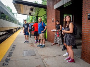 Teens and a professor wait on the platform at the train station.