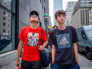 Two students, one in red and the other in blue, look up at NYC skyscrapers.
