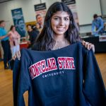 A smiling female student holds up a Montclair State University sweatshirt.