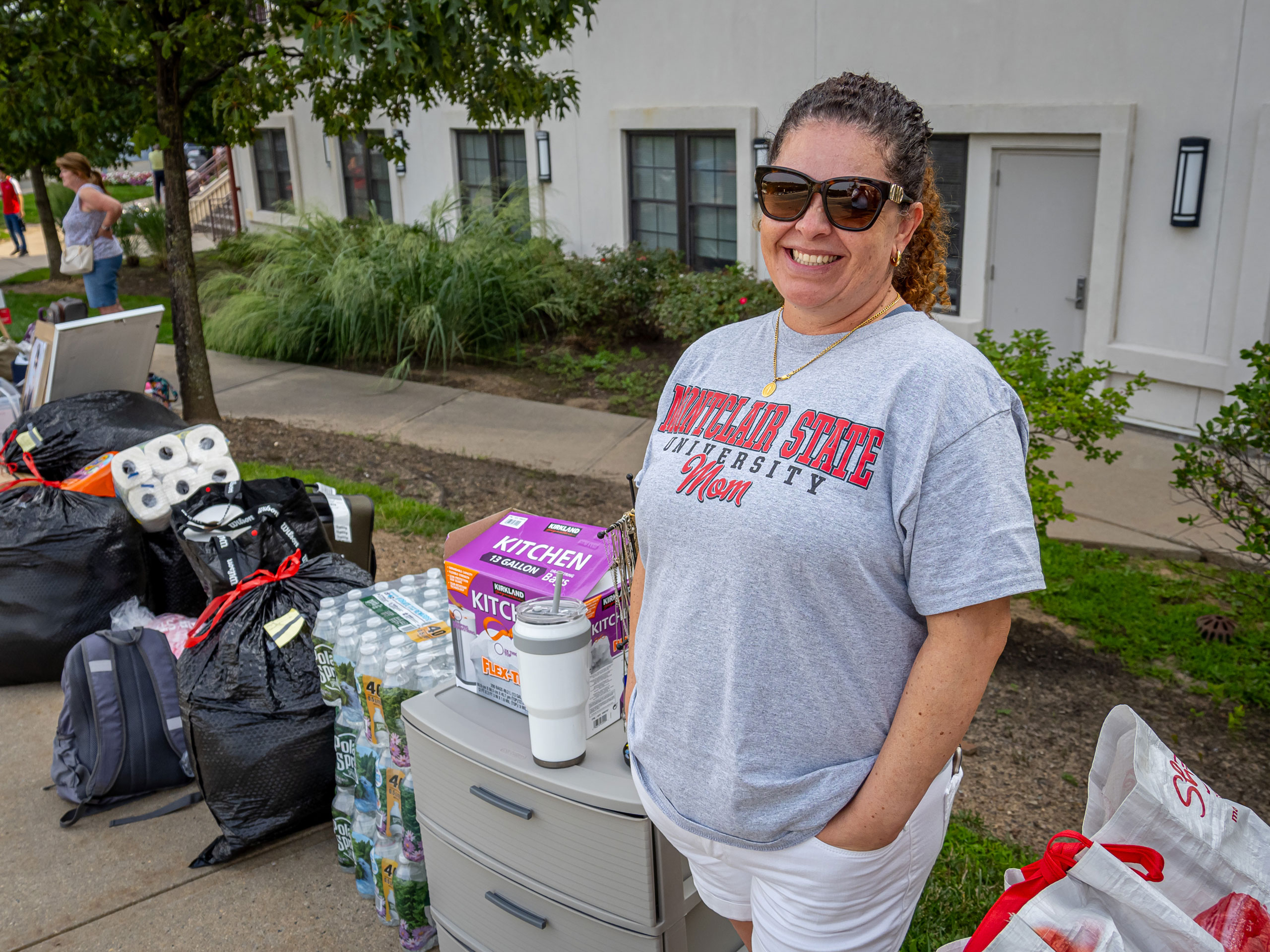 A woman wearing a Montclair "Mom" t-shirt smiles next to a row of residential supplies.