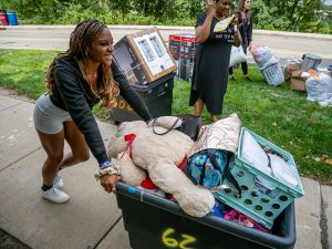A young woman smiles as she pushes a cart filled with personal belongings.
