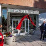 Three people pull down a cover to reveal the Irvin D. Reid Hall sign