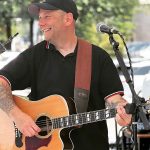A man in a ball cap playing the guitar smiles onstage.