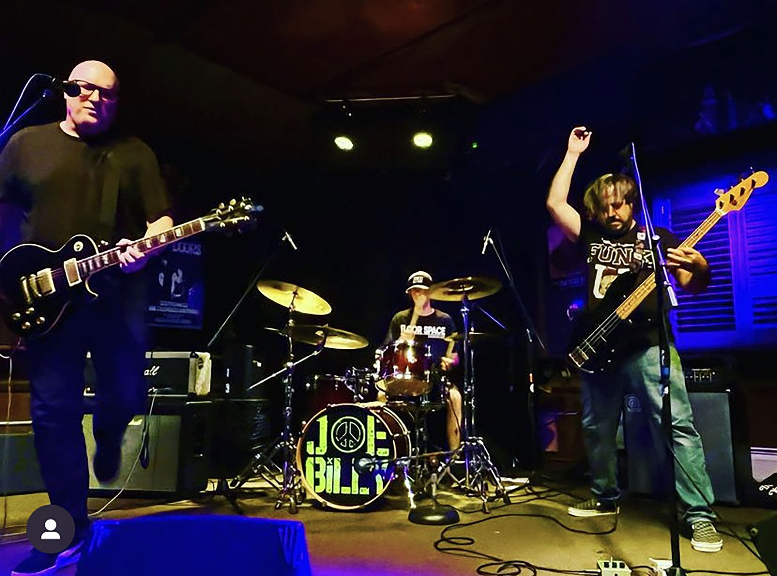 Two guitarists and a drummer perform on stage.