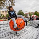 A young woman rides a mechanical pumpkin.