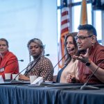 A man at a table gestures as three women look on.