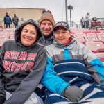 Three people sit in the stands with blankets.