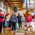 Rocky the Red Hawk mascot plays cornhole with students.