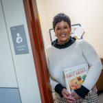A student stands holding books in a lactation room doorway.