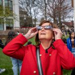 A woman in red wears eclipse glasses to see the sun.