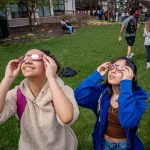 Students with solar eclipse glasses look up, one smiles.