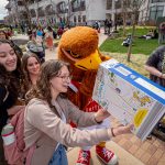 Students and a mascot look in a cereal box made as a solar pinhole viewer.
