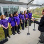 A school choir, wearing purple shirts, sings.