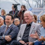 People smile and clap as camera crews look on.