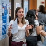 A student gestures as she discusses her research poster.